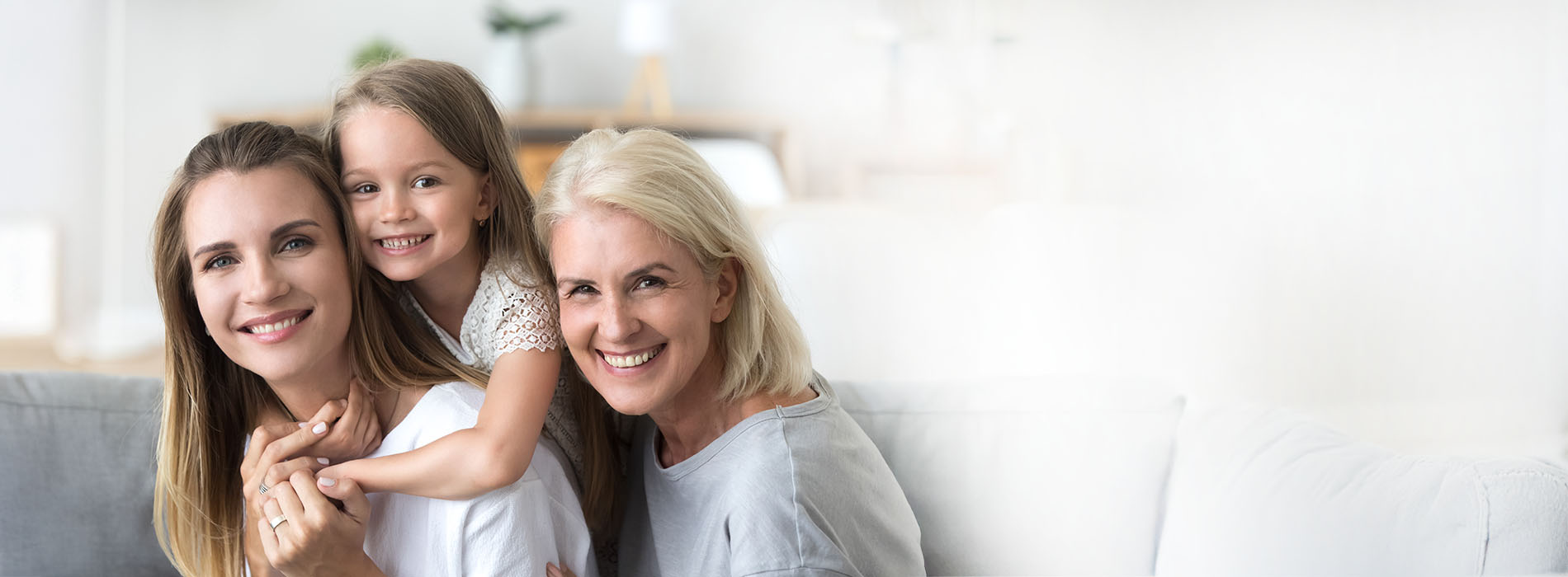 The image shows a family, including a woman, a child, and another adult, sitting together on a couch with a warm and happy atmosphere.