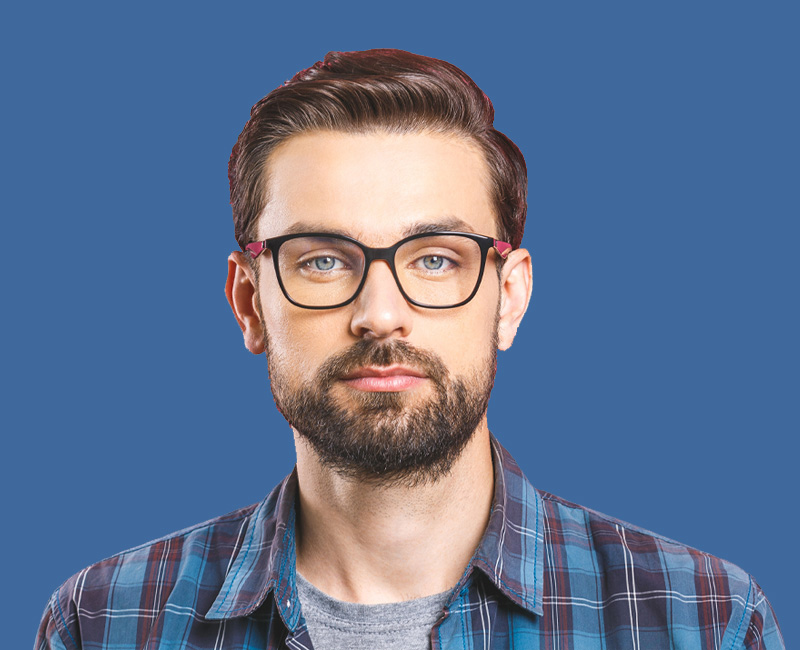 The image shows a man with a beard, wearing glasses and a plaid shirt, posing for the camera against a blue background.